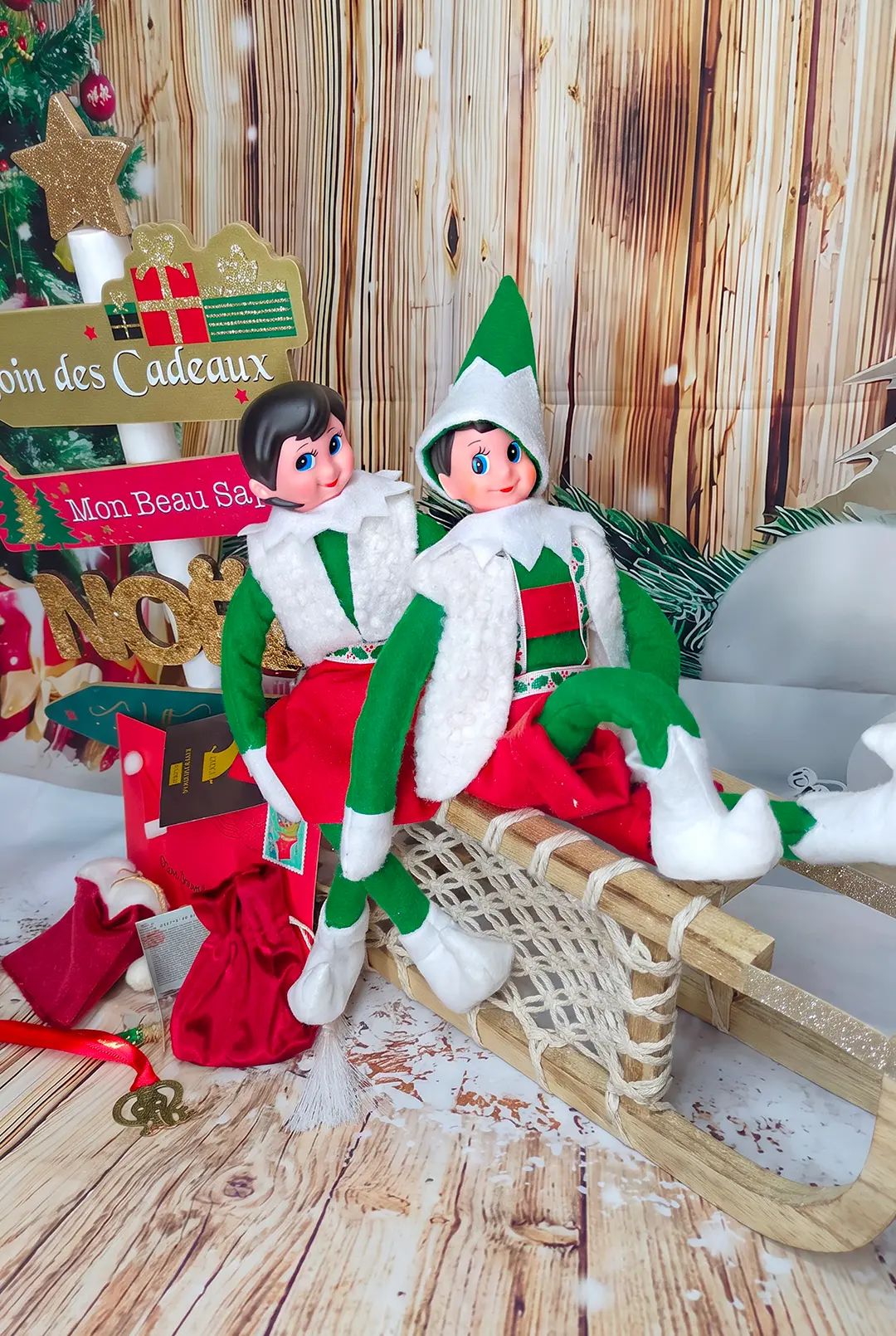 Deux Lutins Farceurs® assis sur une luge, au milieu des cadeaux